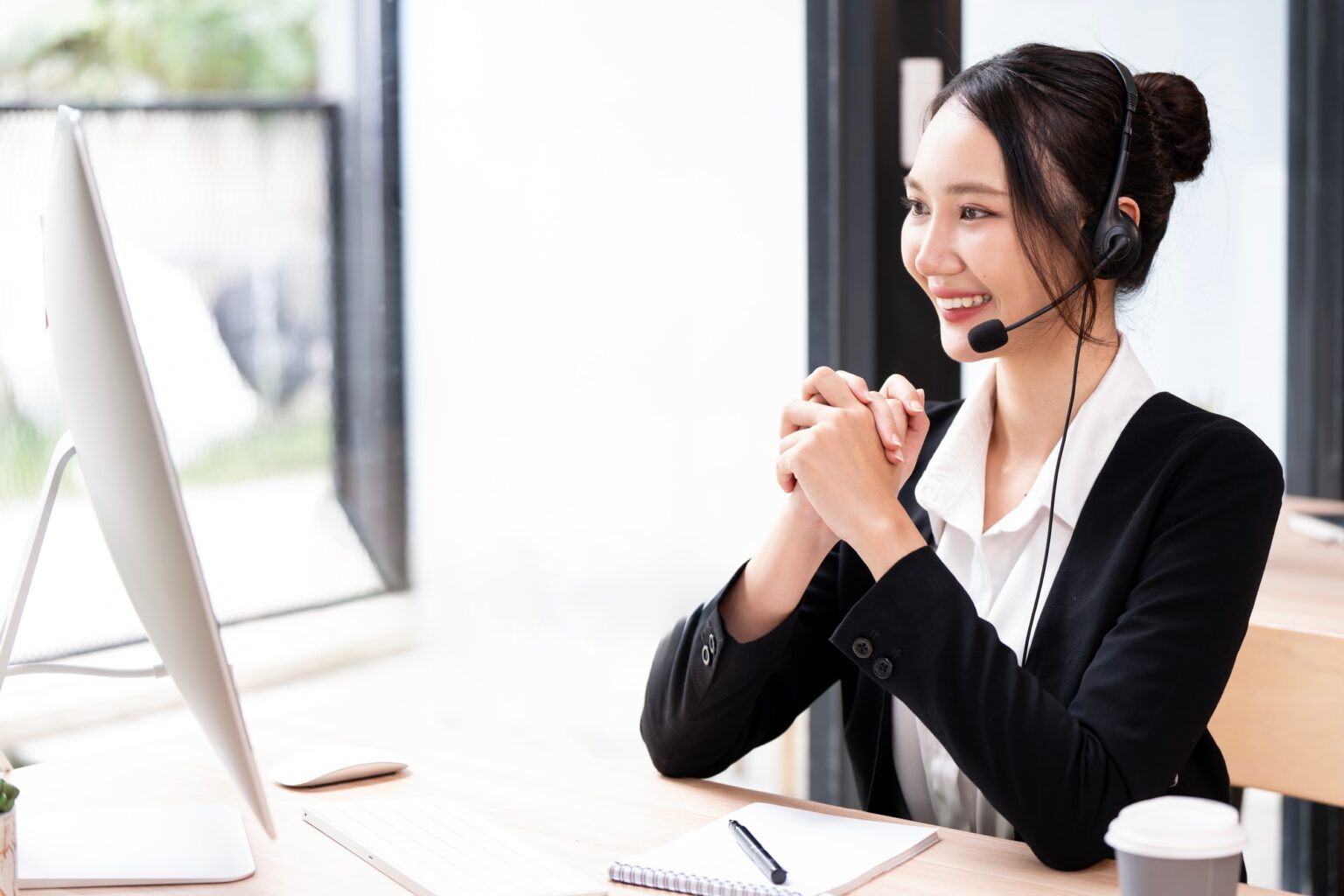 A customer service representative, wearing a headset, smiles and looks at a computer monitor.